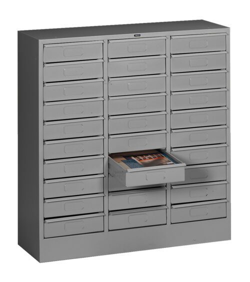 A gray metal storage cabinet with multiple small drawers arranged in rows. One drawer is partially open, containing magazines.