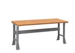 A sturdy workbench with a light brown wooden top and gray metal legs. The legs have reinforced bars for stability. The bench is shown on a plain white background.