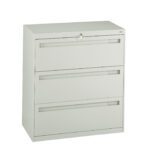 Metallic gray filing cabinet with three horizontal drawers. A lock is visible at the top center, with a key inserted. The cabinet stands on a flat surface against a plain white background.