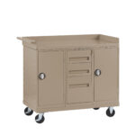 Tan metal utility cart with two large cabinets on each side, two small drawers and one medium drawer in the center. The cart has a flat top with a raised edge on three sides and is equipped with four caster wheels for mobility.