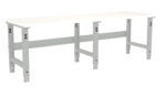 A long, white workbench with adjustable metal legs. The bench has a simple, sturdy design, suitable for various tasks in a workshop or garage setting.