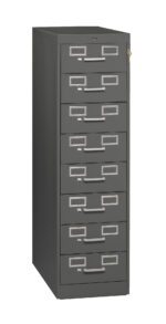 Tall, dark gray file cabinet with six drawers, each featuring a rectangular label holder and handle. A small lock is visible on the top drawer. The cabinet stands on a plain white background.