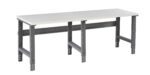 A long, rectangular table with a white tabletop and sturdy gray metal legs. The design features adjustable legs and a support bar underneath for added stability.