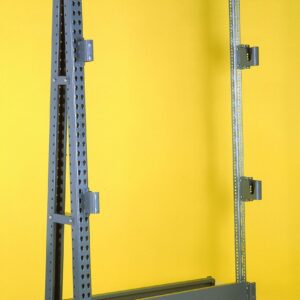 A metal rack structure stands against a bright yellow background. The frame is made of gray, perforated metal beams with crossbars, joints, and brackets, suggesting its a shelving or storage unit.