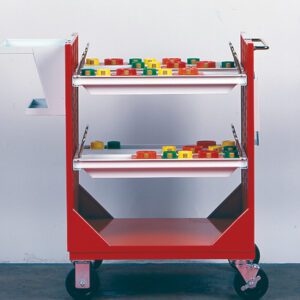 A red utility cart with two shelves, each holding colorful, rectangular objects. The cart has wheels for mobility and a white attachment on one side. The background is a plain white wall with a gray floor.