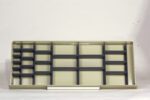 Empty beige shelving unit laid horizontally against a white background. The unit has multiple rows with dark gray dividers and a clean, minimalist design.