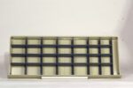 Empty beige shelving unit with a grid of rectangular compartments against a plain white background. A white cylindrical object is resting at the base of the unit.
