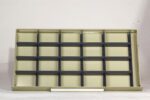 An empty beige display shelf with multiple rows and columns of compartments, aligned against a plain white background. The shelf has dark horizontal dividers and is designed for organizing items.