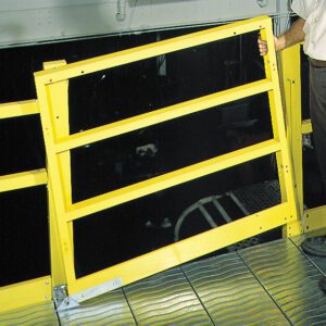 A person wearing pants and holding onto a bright yellow safety rail by a metal walkway. The surrounding area is industrial, home to customizable shelving systems with a dark space beyond the railing.