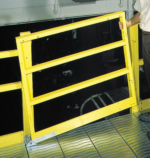 A person wearing pants and holding onto a bright yellow safety rail by a metal walkway. The surrounding area is industrial, home to customizable shelving systems with a dark space beyond the railing.