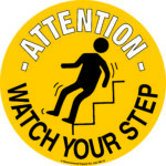 A 430mm yellow circular sign shows a black silhouette of a person slipping on stairs with bold Attention and Watch Your Step similar to MH-USA Floor Graphic Markers - 16.93 in. dia. for enhanced safety.