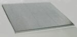 Image of a single sheet of transparent or frosted glass resting on a flat, light-colored surface. The glass has a subtle texture and reflects light slightly.