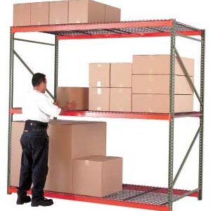 A person arranges large brown cardboard boxes on a red and gray metal shelving unit beside wire mesh cages. The shelves are partially filled, and one large box is placed on the floor. The background is plain white.