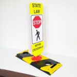 The TCT Flexible Post Crosswalk System, State Law - Stop, includes a yellow and white sign with a red stop sign icon above a figure walking labeled Within Crosswalk, and it is mounted on a black and yellow base for better visibility.