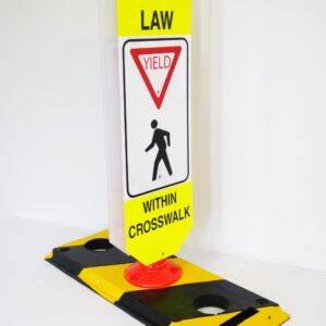 The TCT Flexible Post Crosswalk System, State Law - Yield features a sign on a yellow/black base that reads State Law: Yield to Pedestrians Within Crosswalk, with a pedestrian symbol and yield triangle, set against a plain white background for enhanced visibility.