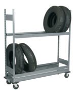A gray metal shelving unit on wheels holding four car tires. Three tires are on the bottom shelf, one propped up against two lying flat, and one tire is on the top shelf, placed upright. The unit is in an empty space.