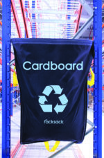 A blue MH-USA Racksack - Cardboard with a recycling symbol hangs on a rack in the warehouse, surrounded by industrial shelves and bright lighting.
