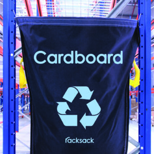 A blue MH-USA Racksack - Cardboard with a recycling symbol hangs on a rack in the warehouse, surrounded by industrial shelves and bright lighting.