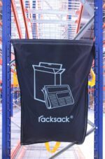 A blue MH-USA Racksack for Mixed Paper and Card hangs on a warehouse metal shelf, featuring a white cardboard box and newspaper icon with yellow side handles.
