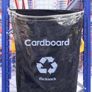 Hanging on a metal rack surrounded by industrial beams and shelves, the black MH-USA Racksack Clear - Cardboard boldly displays a recycling symbol and the word Racksack.
