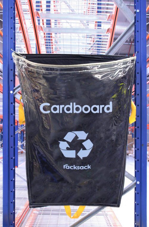 RSCL1-C.jpg Hanging on a metal rack surrounded by industrial beams and shelves, the black MH-USA Racksack Clear - Cardboard boldly displays a recycling symbol and the word Racksack.