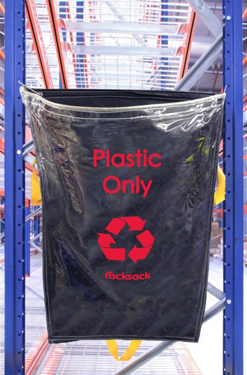 RSCL1-P.jpg A blue and black MH-USA Racksack Clear - Plastic Only bag hangs on a metal rack in a warehouse. It displays a red recycling symbol and racksack at the bottom, with orange-beamed shelving and metal grating visible in the background.