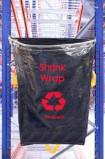 A black rucksack labeled Shrink Wrap with a red recycling symbol elegantly hangs on blue metal shelves, clearly marked as MH-USA Racksack Clear - Shrink Wrap.