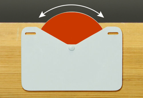 SIW_02.jpg A red semicircle MH-USA Stock Indicator Wheel, part of a pack of 10 self-adhesive units, peeks over a wooden surface, partially obscured by a white card with rounded edges and slotted holes for adjustability. An arrow shows the semicircles range of motion.