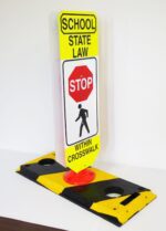 The TCT Flexible Post Crosswalk System features a yellow and black sign with School State Law - Stop Within Crosswalk, including a red stop sign graphic over a walking figure, mounted on a robust black and yellow base.