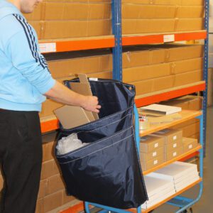 In a storage area, someone in glasses and a blue jacket arranges flat boxes into a covered MH-USA Racksack Trolley - Double Pocket. Behind them are shelves of neatly stacked cardboard boxes.