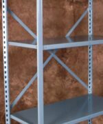 A gray metal shelving unit with three customizable shelves stands against a brown textured background. The heavy-duty parts storage solution features supportive cross-bracing at the back, making it perfect for organizing even the toughest powersports inventory.