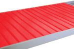 A metallic red roof panel with a ribbed design is shown. The panel features parallel raised ridges and a smooth finish, bordered by a silver edge.