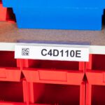 On a shelf, a red storage bin labeled C4D110E features an MH-USA Angled self-adhesive Ticket Holder. A partially visible blue bin sits above it. A QR code on the labels left side highlights efficient organization in action.