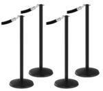 Four Visiontron Prime Flat Top Stanchion Bundles with retractable belts are set in a simple line. The stanchions, equipped with a round base, are perfect for crowd control or queuing.