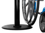A shiny silver wheelchair wheel is positioned next to a Visiontron Value Series Black Steel Retractable Belt Stanchion with a 7.5 belt, set against a white background to highlight their contrasting elements.