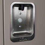 Close-up of a rectangular recessed metal handle on a locker door, featuring a round lock and two rivets. The word LYON is embossed at the bottom of the handle. The handle has a sleek, brushed metal finish.