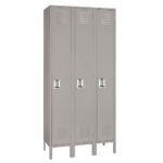 A set of three tall gray metal lockers, each with a vented door and a handle. The lockers are standing side by side, elevated on short legs.