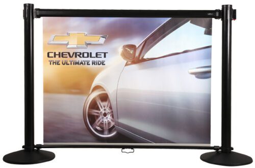 A Chevrolet ad shows a close-up of a silver car with the Chevrolet logo and The Ultimate Ride slogan, beautifully set against a blurred backdrop on the sleek Retracta-Banner Panel System with two sturdy black posts.