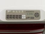 A close-up of the Metro FLX420 Flexline Advanced LCD Keyless Entry Touchpad shows a keypad with numbers and function buttons like ENTER and LOCK CLEAR, plus a digital display reading 1:34 PM. It features Auto Lock and is mounted on a white surface.