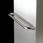 Close-up of a silver metal grab bar like the Metro C5-RHANDLE Rear Push Handle for C5 1 Series Cabinets, mounted on a light gray wall against a black backdrop. The horizontally aligned handle is secured with multiple screws, subtly reflecting light.