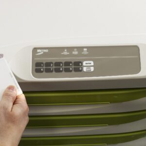 A hand holds a white card near a numeric keypad on a green Metro FLX430PHF Flexline cabinet. The pad, featuring 0-9, Enter, and Lock/Close buttons, operates with the High Frequency Proximity Cart Reader for secure access.