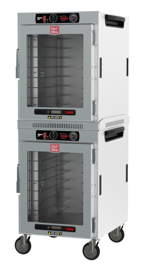 The Metro HBCW16-AC-M HotBlox is a 16-pan insulated dual-cavity stainless steel holding cabinet with clear doors, analog controllers, and NEMA 5-15P. It features control dials, temperature gauges, and wheels for mobility.