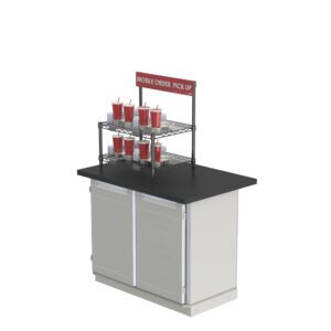 The Metro CR1824TG2B Countertop Order Pickup Station, featuring a sleek black counter and light gray base with doors, is set with red cups and straws. A sign above reads: Mobile Order Pick Up.