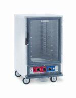 The Metro C515-CFC-UA C5 1 Series is a commercial stainless steel warming cabinet on wheels with a transparent front door. It features red and blue dials on the bottom control panel for temperature settings and includes universal wire slides with multiple interior tray racks, compatible with 120V, 60Hz power supply.