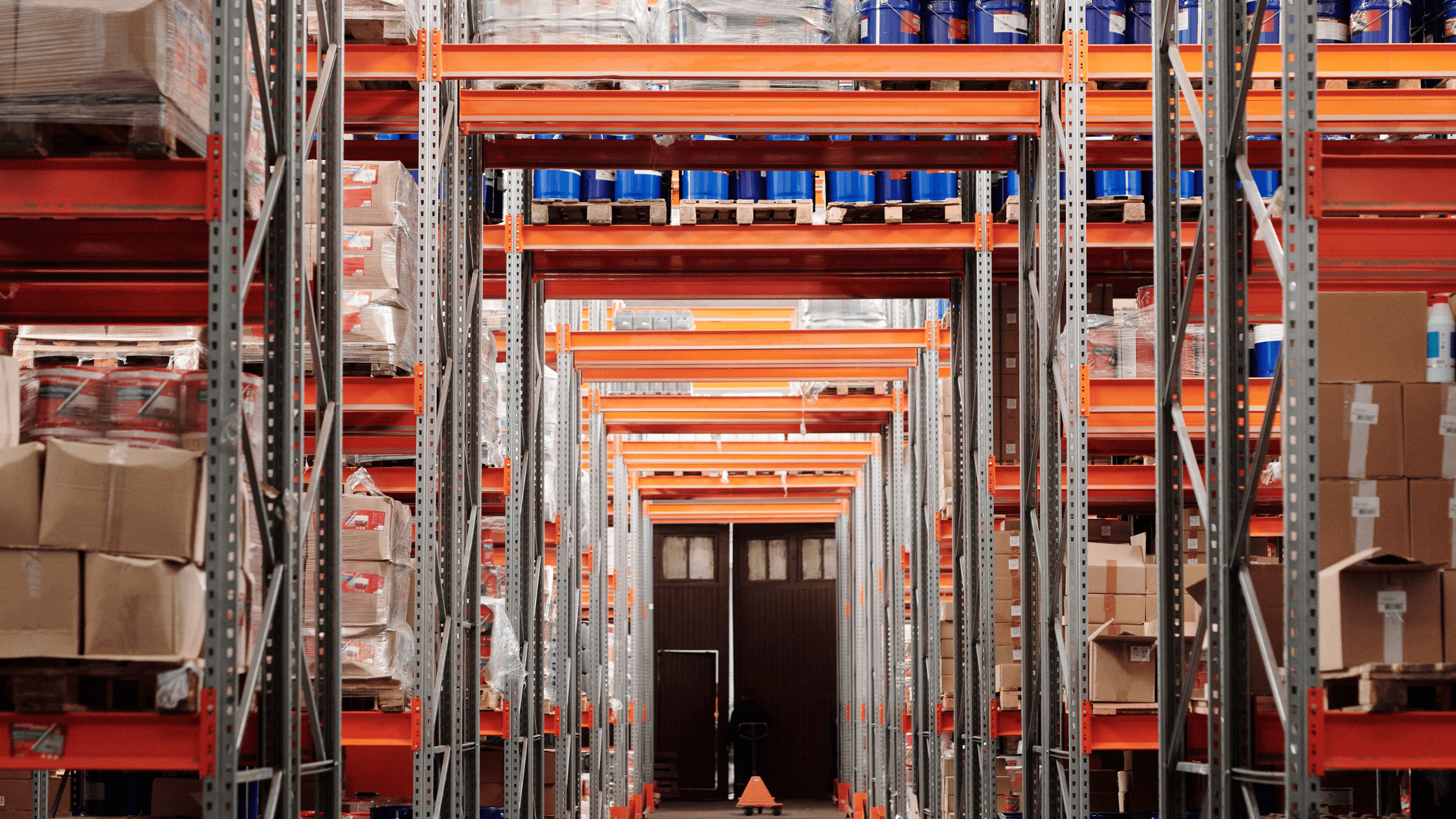 Long aisle of steel shelving and rack bays holding boxed parts in a parts warehouse