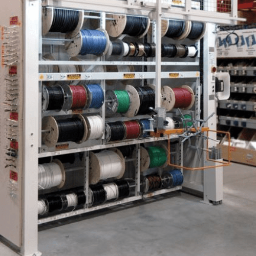Shelves with large spools of various colored wires showcase industrial storage solutions in a hardware store. A user-friendly mechanical dispenser simplifies wire distribution. The concrete floor adds to the low-maintenance setup, while other store shelves are partially visible in the background.