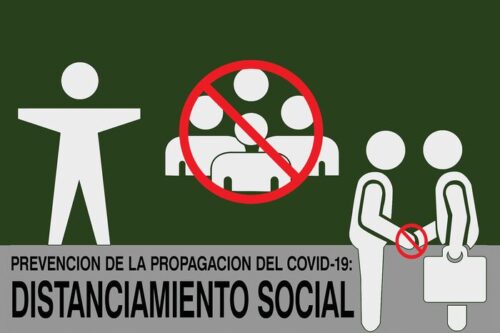 A red symbol on the Justrite Mat,194 Span Social Distan 4X6 prevents gatherings and handshakes between two figures. The text reads Prevención de la propagación del COVID-19: Distanciamiento Social against a green backdrop.
