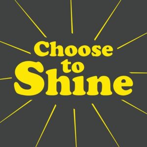 The Justrite Mat product, featuring Choose to Shine in bold yellow text on a dark gray background, displays yellow rays creating a sunburst effect that embodies positivity and inspiration.