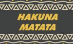 The image depicts the Justrite Mat, version 195 Hakuna Matata 3X5 Ch, featuring bold yellow letters on a dark background with triangular patterns and light-colored circles.