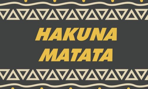 The image depicts the Justrite Mat, version 195 Hakuna Matata 3X5 Ch, featuring bold yellow letters on a dark background with triangular patterns and light-colored circles.
